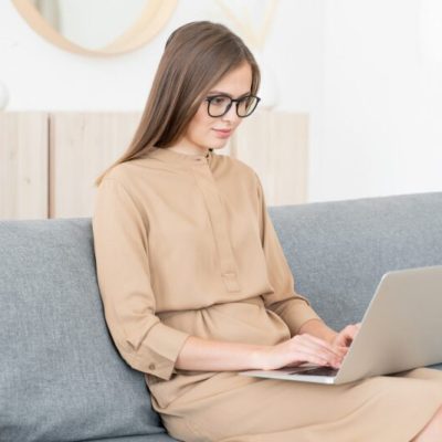 Young business woman sitting on sofa with open laptop, working from home